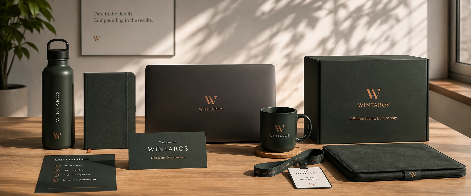 Wintaros-branded items laid out on a desk: a water bottle, a notebook, a laptop, a mug, a welcome card, a lanyard with an ID card, a box and a folio.